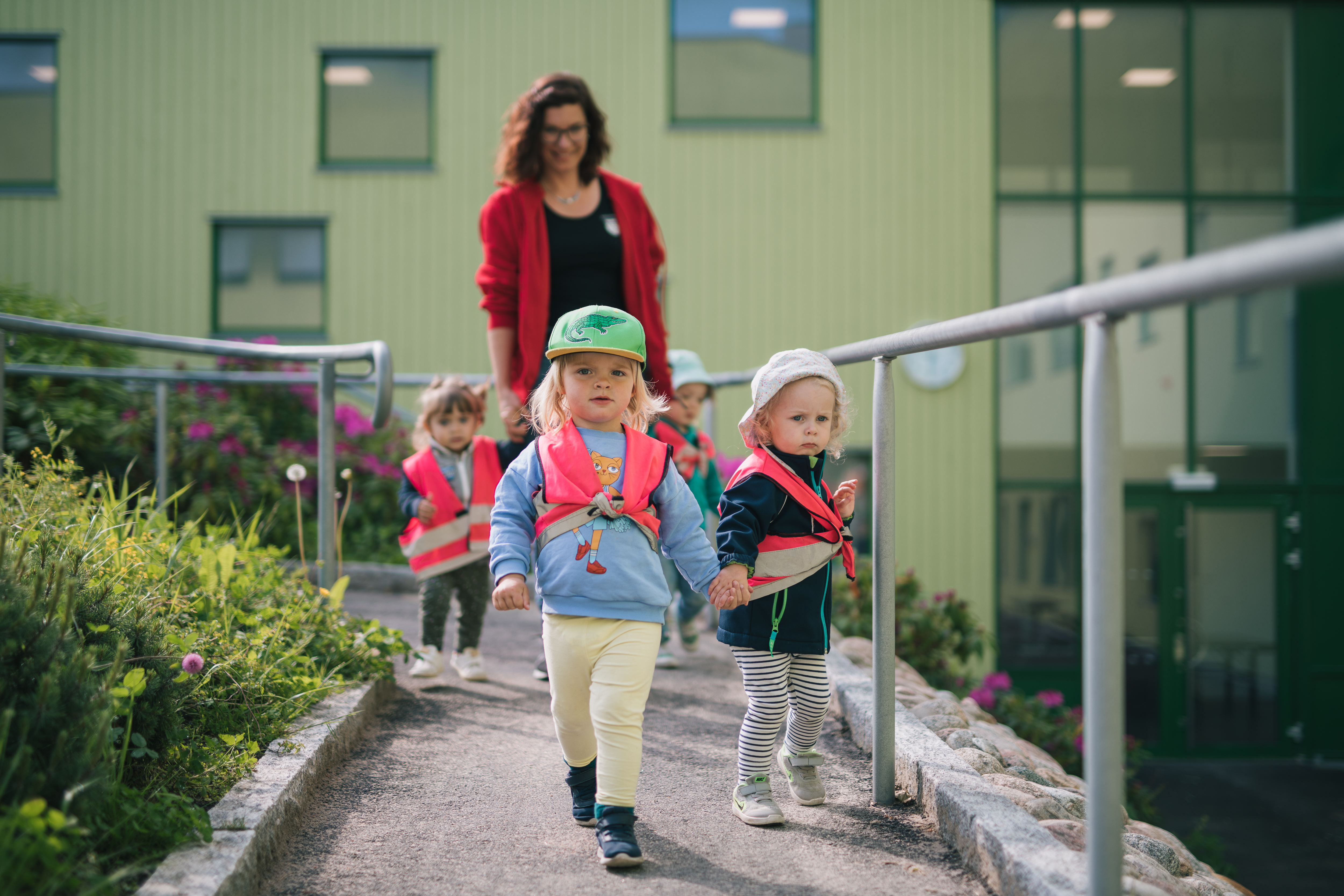 Tre barn i förskoleåldern med rosa reflexvästar är ute tillsammans med förskollärare.