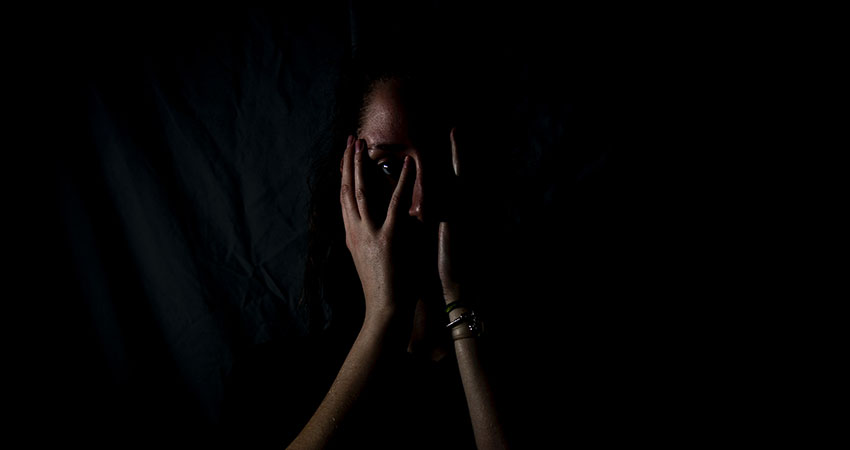 Kvinna håller för sitt ansikte med sina händer med en mörk bakgrund.