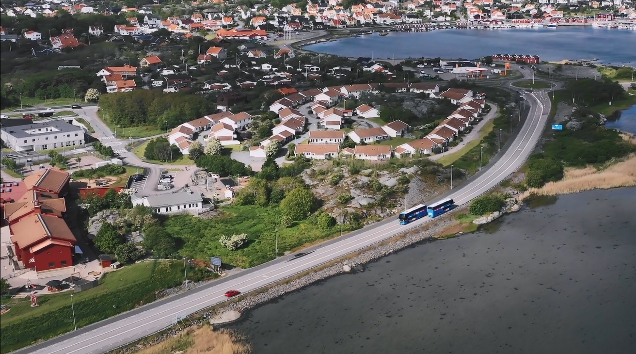 Drönarbild på två bussar som möts på en bilväg. Det är hus, hav och grönt runt om.