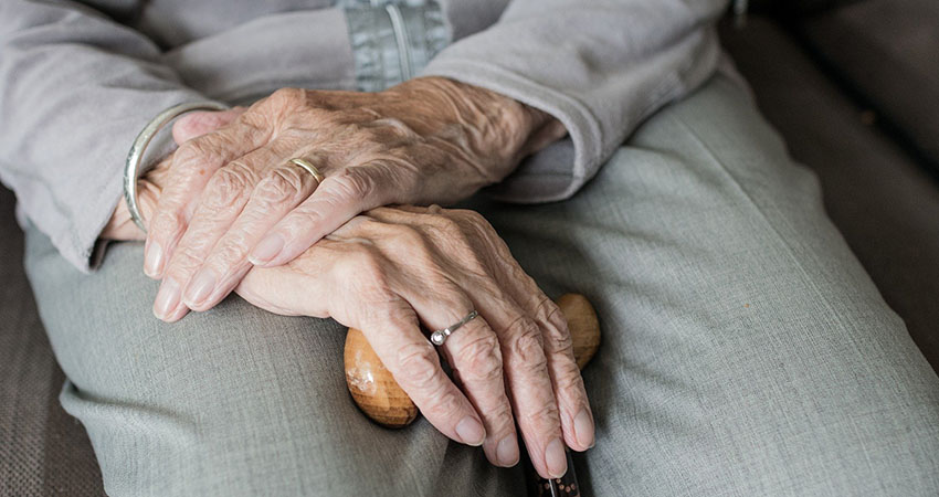 En äldre person sitter och lutar händerna mot en käpp.