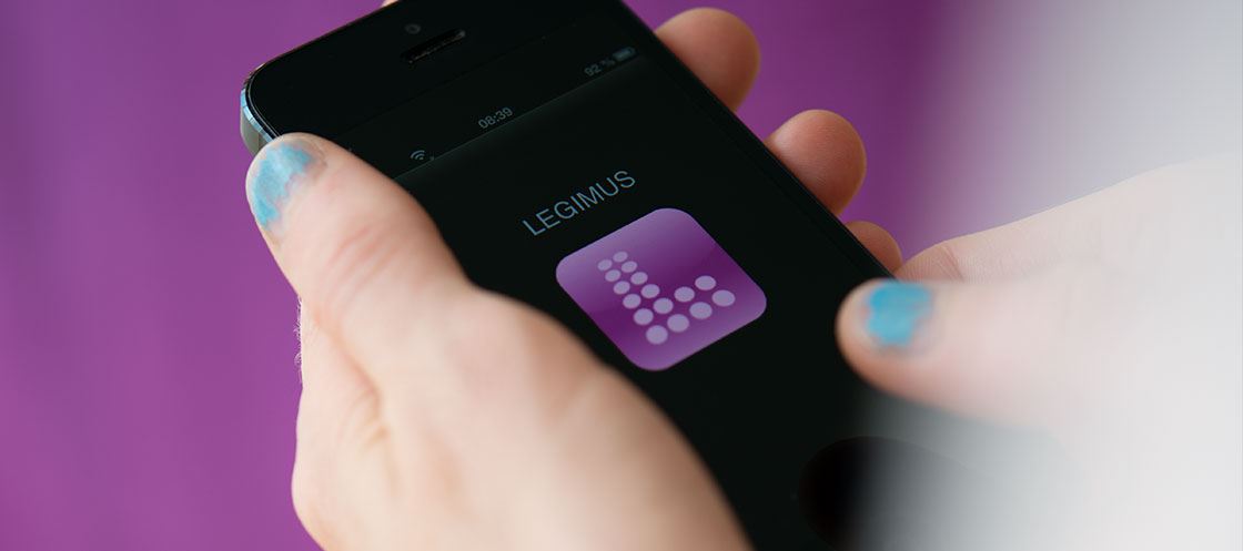 En kvinnohand håller i smartphone med appen Legimus öppen, mot lila bakgrund.