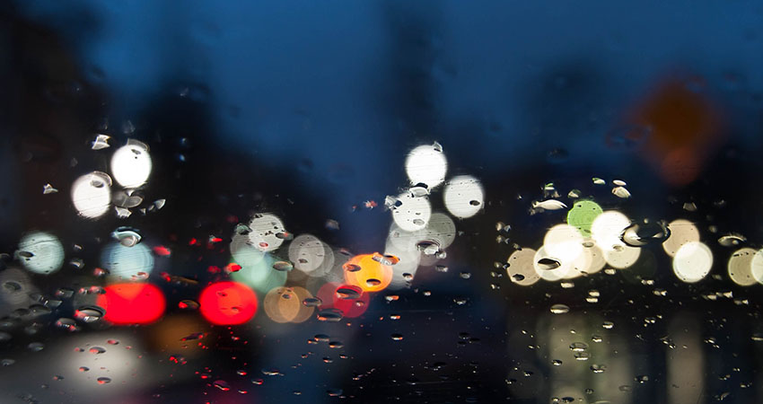 Blurriga regndroppar på en bils framruta i mörkret.