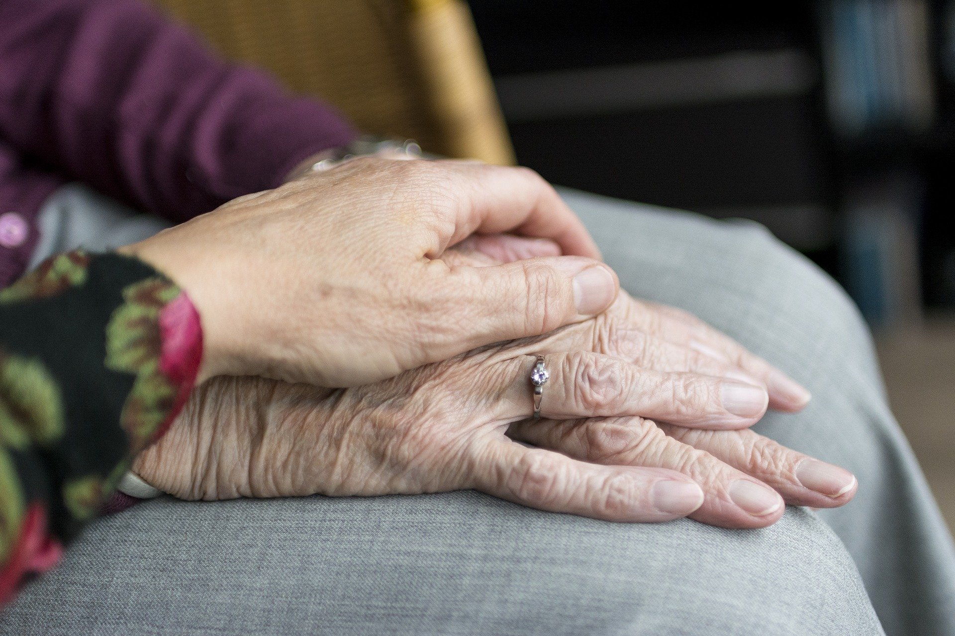 En anhörig lägger handen om en äldre persons hand. Visar trygghet.