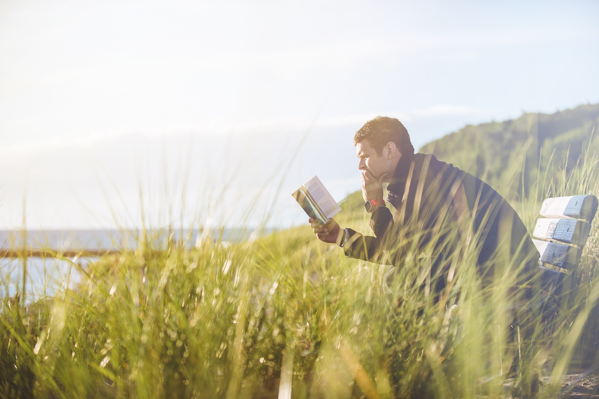 Bilden föreställer en man som sitter i grönskan och läser en bok.