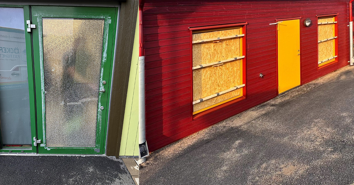 Krossat glas på glasdörr och plywoodskivor istället för fönster på röd byggnad.